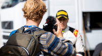 A man records an interview with a rally driver using a handheld camera