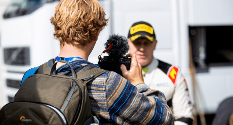 A man records an interview with a rally driver using a handheld camera